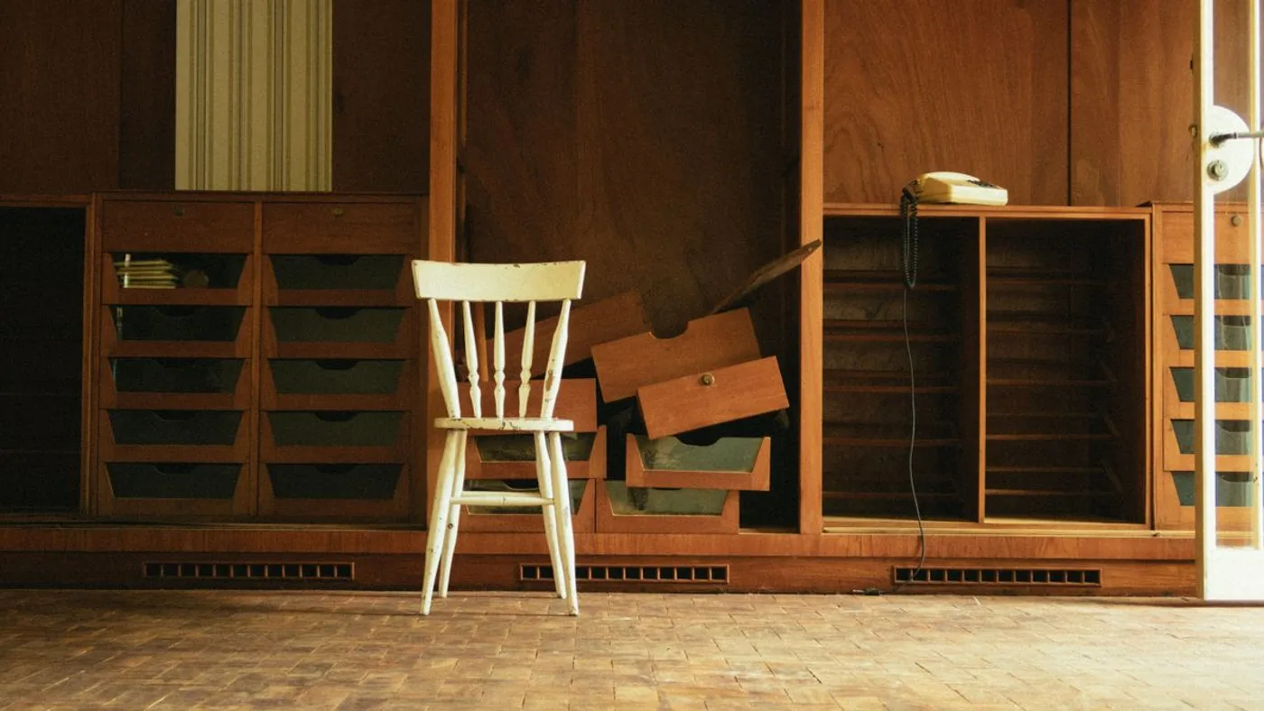 Wall of built-in wooden storage with drawers pulled out and stacked, a wooden chair and an old corded telephone
