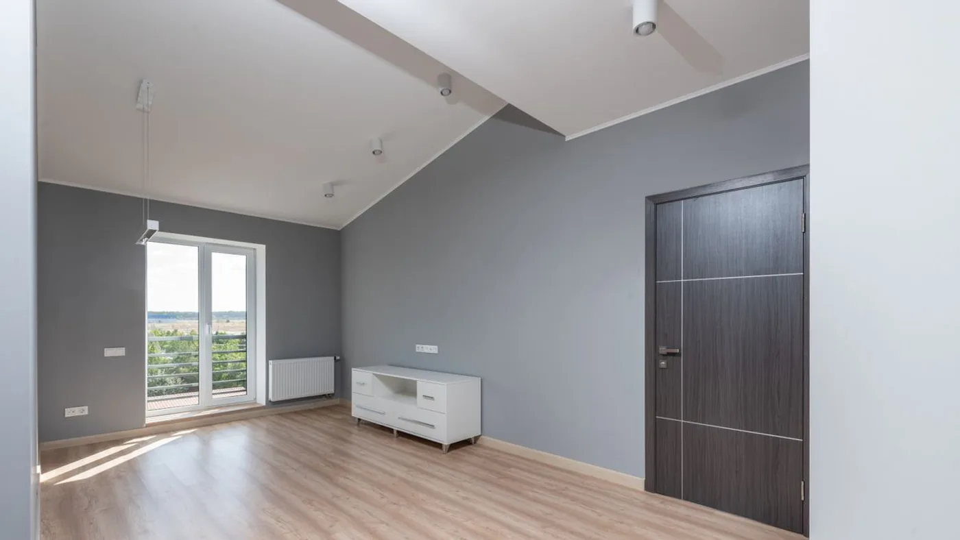 Emptied grey-walled room with wooden flooring and a single low white cabinet left standing against the wall