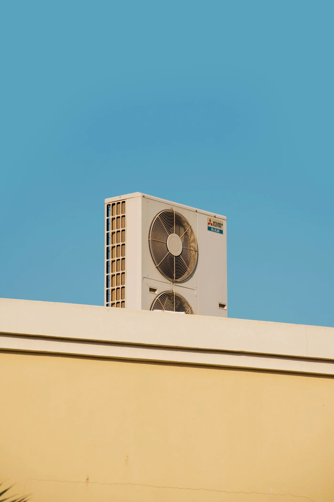 White outdoor air conditioning condenser unit mounted on a rooftop parapet against a clear blue sky