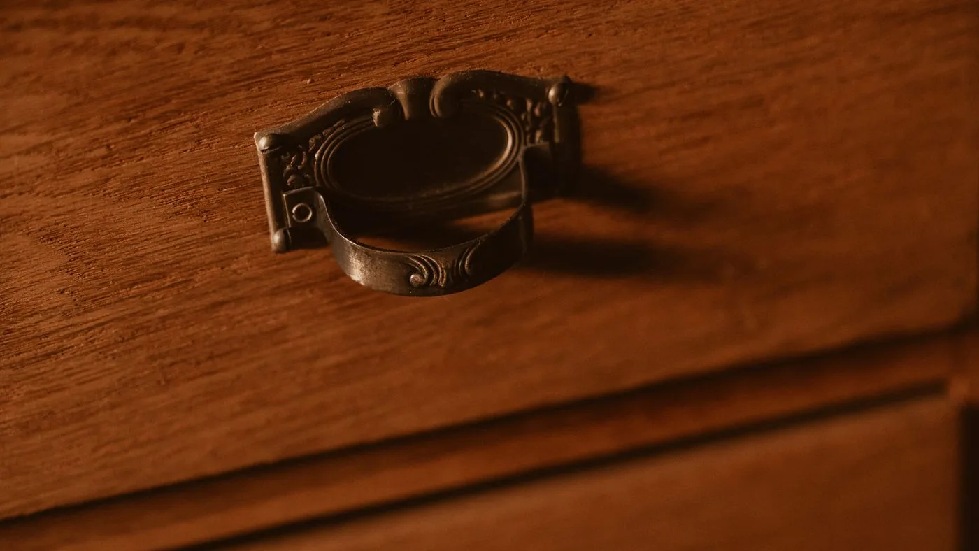 Close-up of an ornate cast brass drop handle mounted on the front of an aged polished wooden drawer