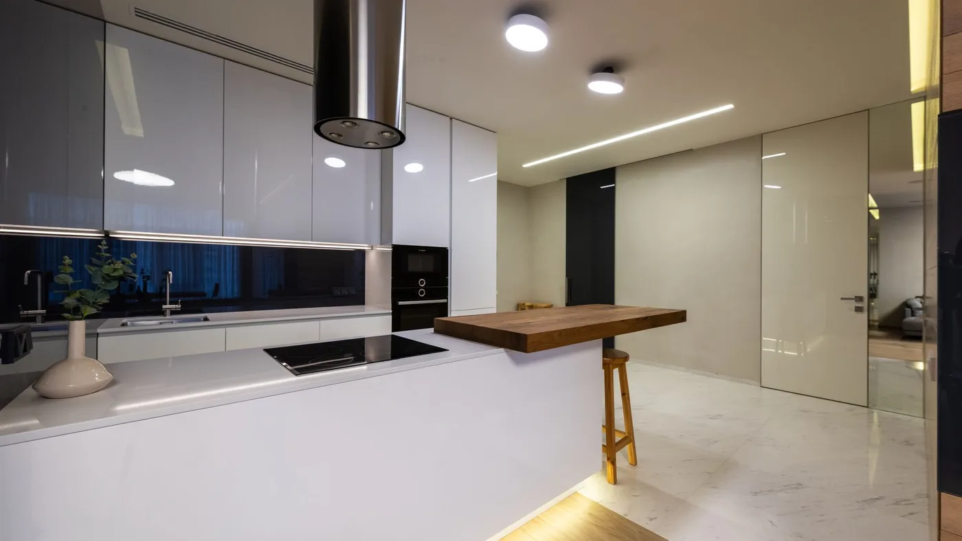 Finished modern kitchen with glossy white cabinetry, a black built-in oven and hob, and marble flooring after a renovation is complete
