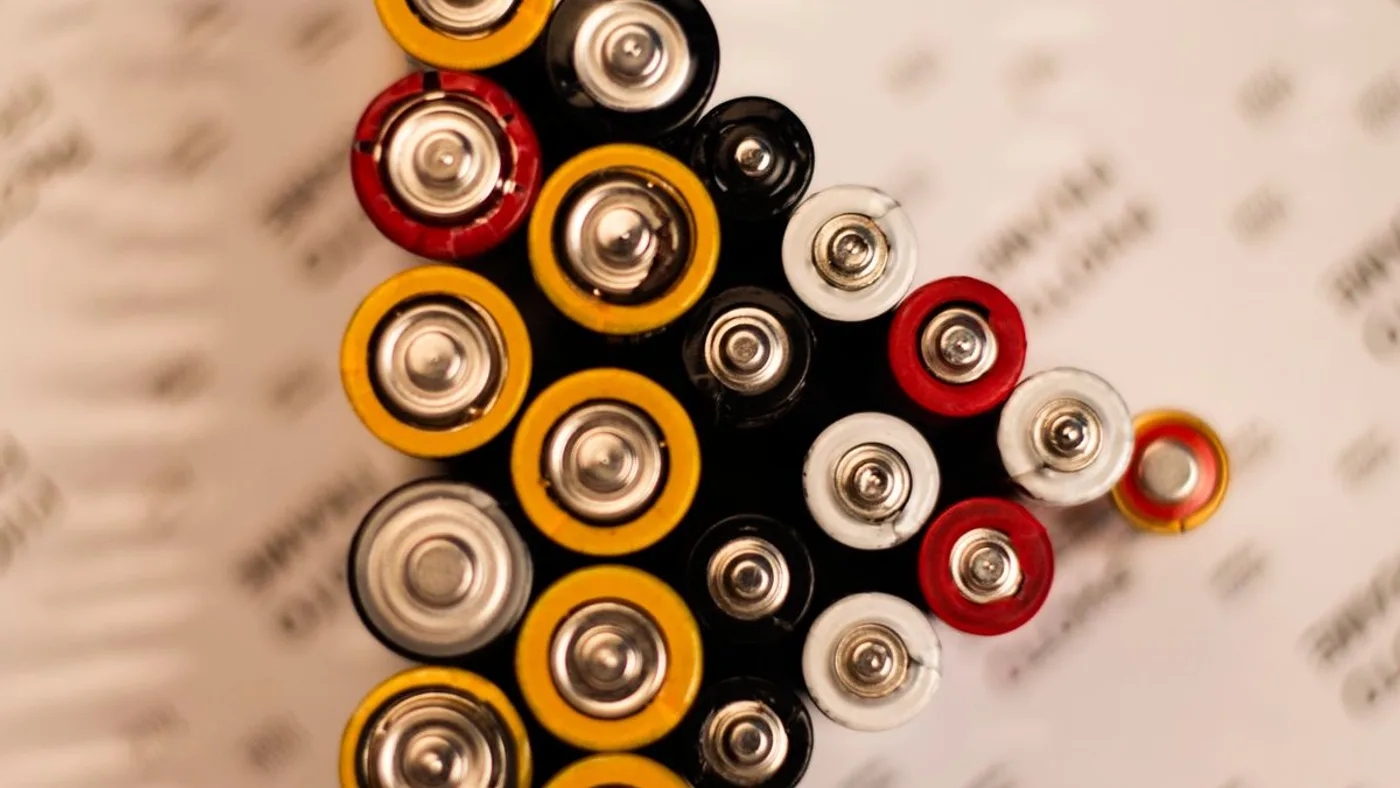 Used AA and AAA batteries in yellow, red, white and black casings laid out in a wedge with their terminals facing up