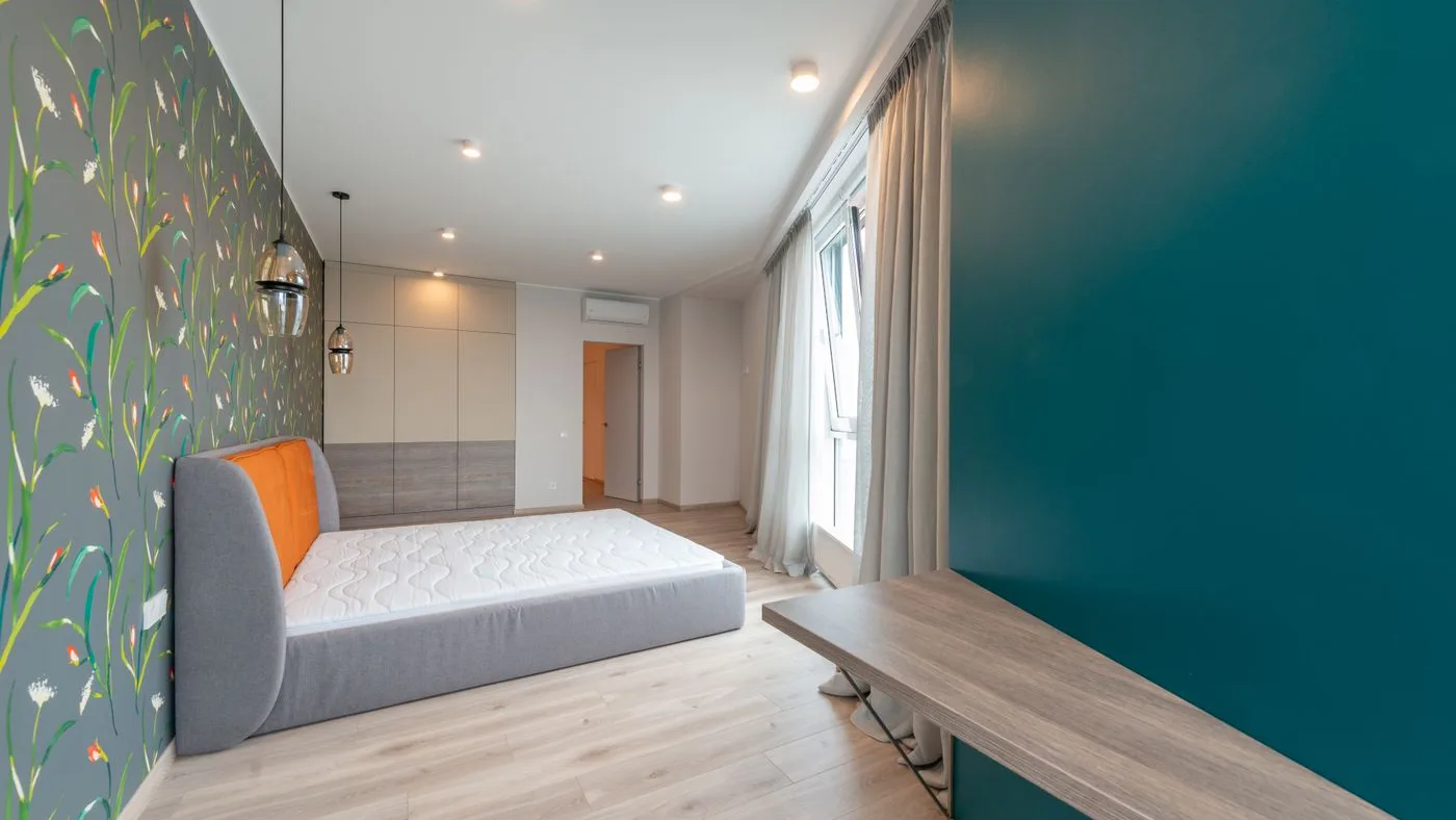 Bare mattress on a grey upholstered bed base in an otherwise empty room with pale wood flooring and fitted wall units