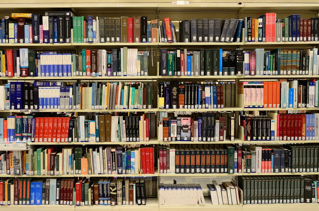 Tall metal shelving unit filled across six levels with densely packed reference books, folders and journals in many colours