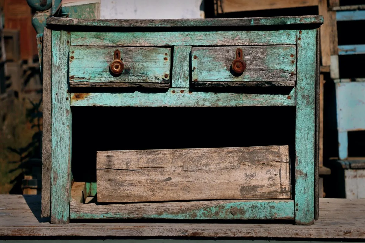 Weathered turquoise painted wooden cabinet with split timber, exposed grain and a broken drawer front hanging loose from its frame