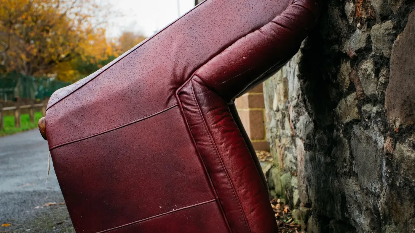Old burgundy leather sofa tipped on its side and left outdoors against a stone wall