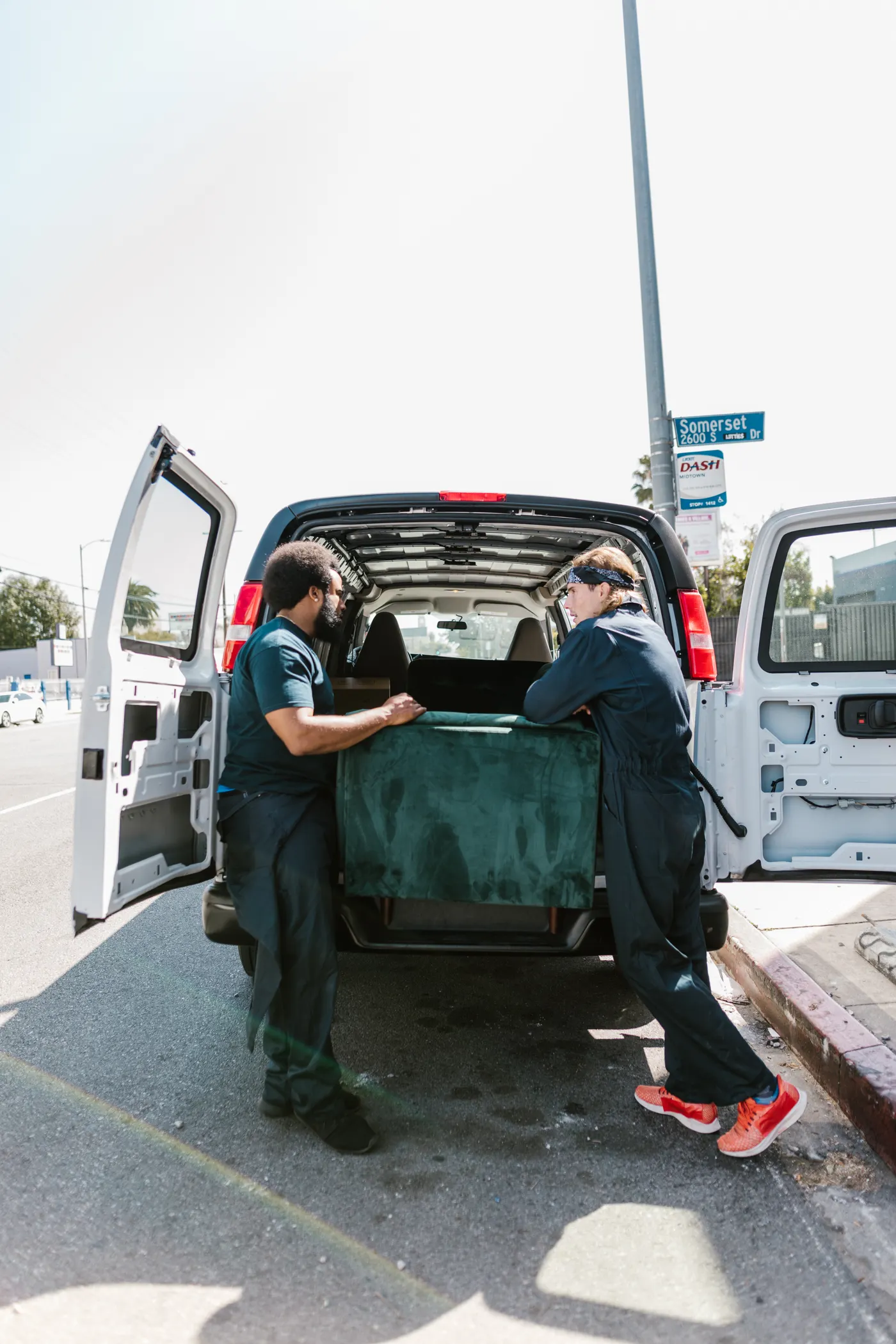 Two uniformed movers loading furniture into a van on a sunny street, representing an affordable junk removal collection in Dubai