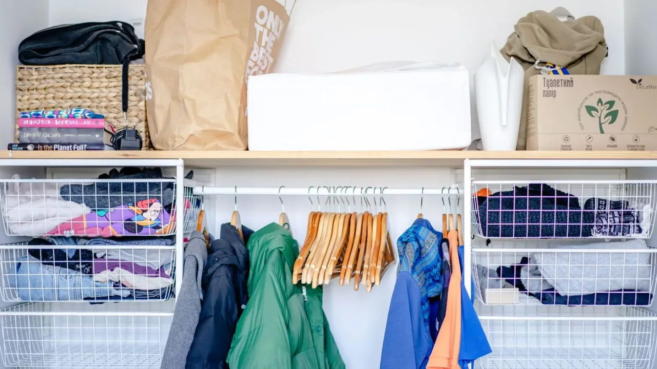 Open wardrobe with hanging clothes, empty wooden hangers, wire baskets and storage boxes