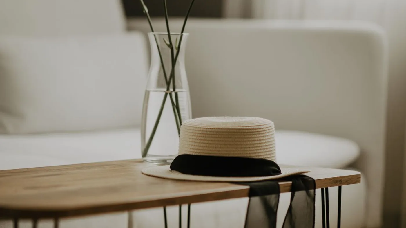 Wooden coffee table with thin black hairpin legs holding a glass vase of flowers and a straw hat, beside a white sofa