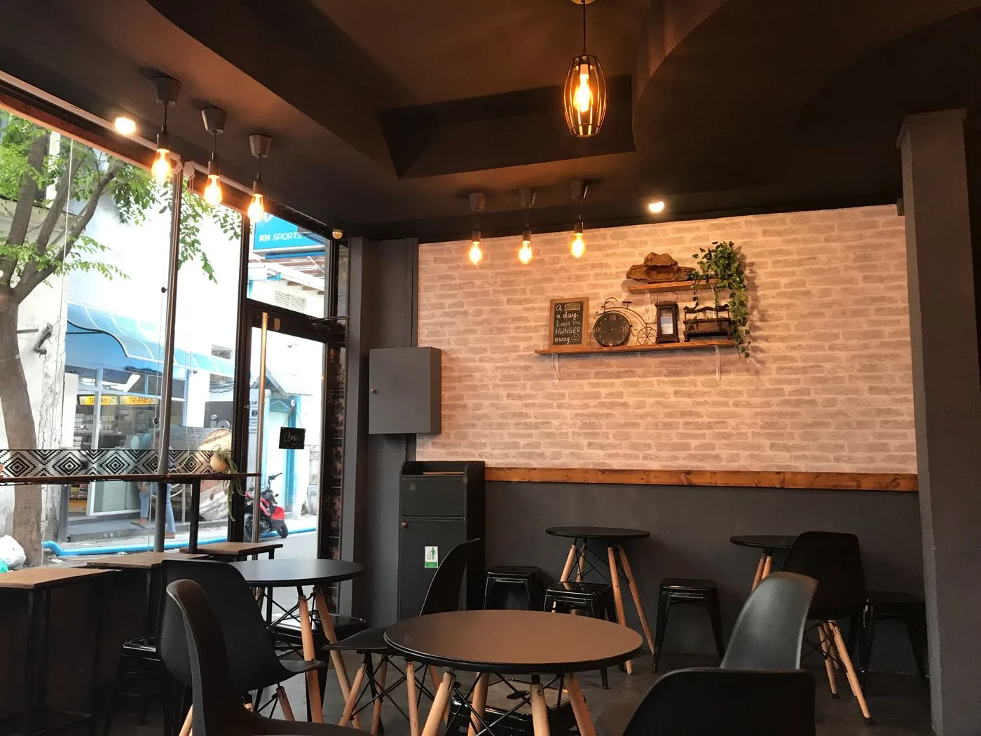 Cafe interior with round black tables, wooden-legged chairs, metal stools and hanging pendant lights
