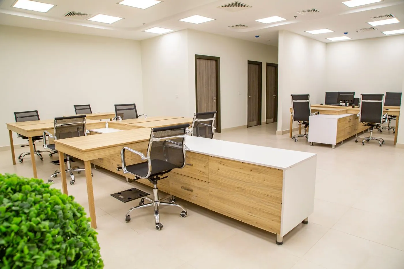 Open plan office with light wooden desks, black mesh chairs and storage units on a tiled floor