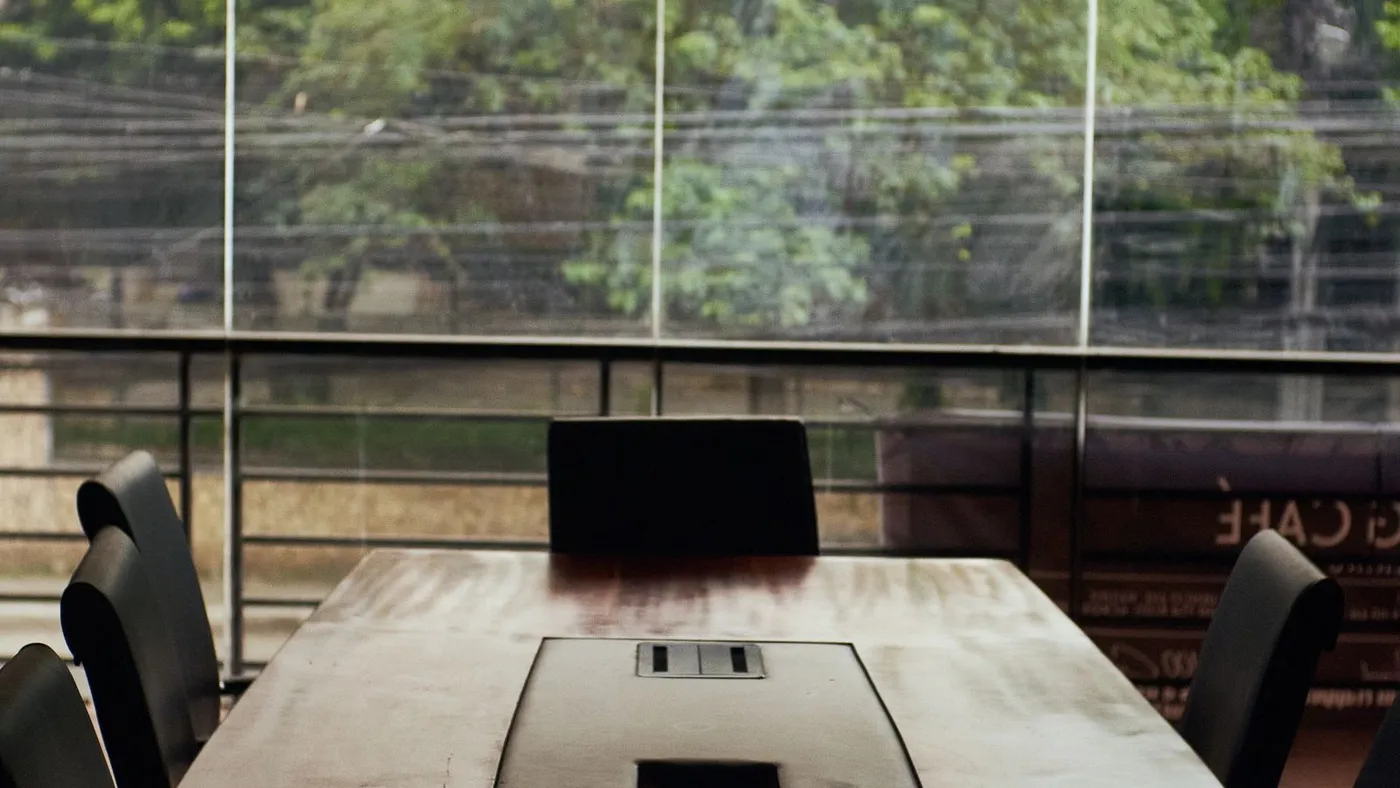 Close-up along a wooden meeting table showing a recessed central metal spine with two flip-up power sockets and a rectangular cable port