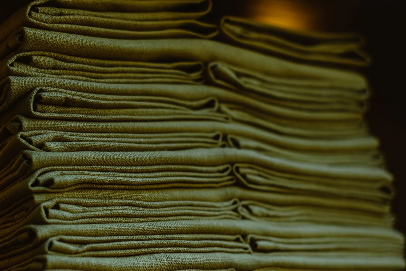 Close-up of many folded lengths of olive linen fabric stacked in a neat pile ready for sorting