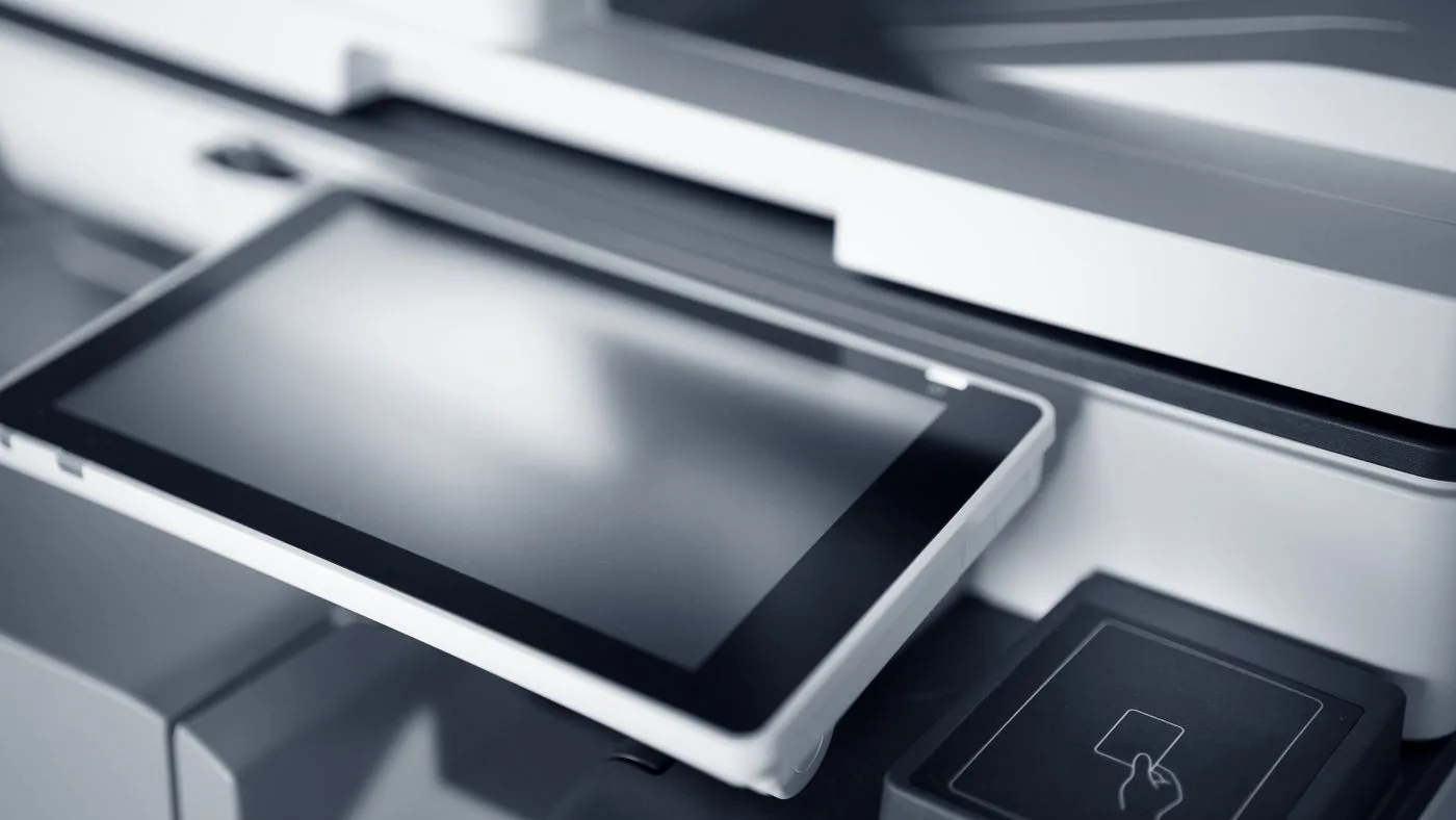 Close-up of a multifunction office printer's tilted touchscreen control panel beside a card reader pad