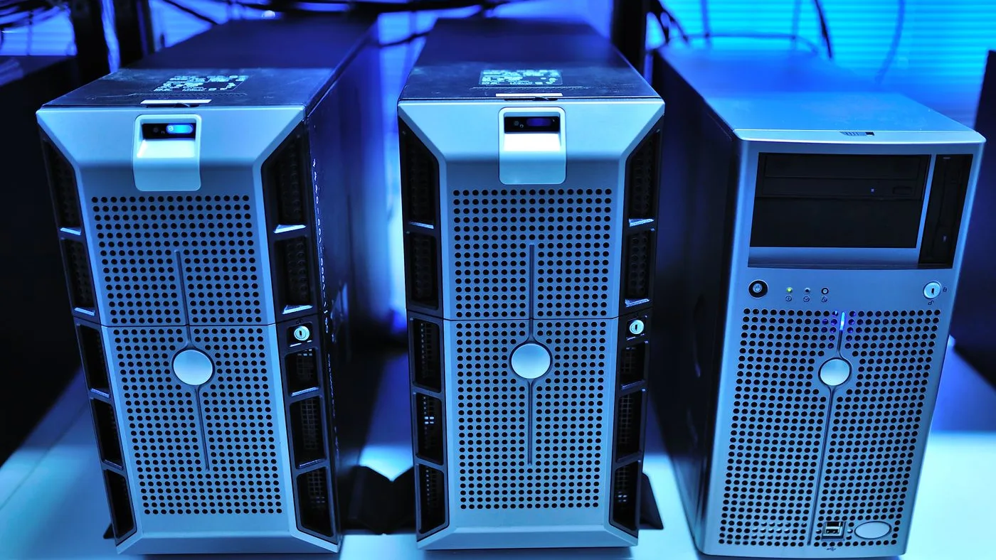 Three tower servers with perforated front panels and lockable bezels standing side by side on a rack shelf under blue lighting