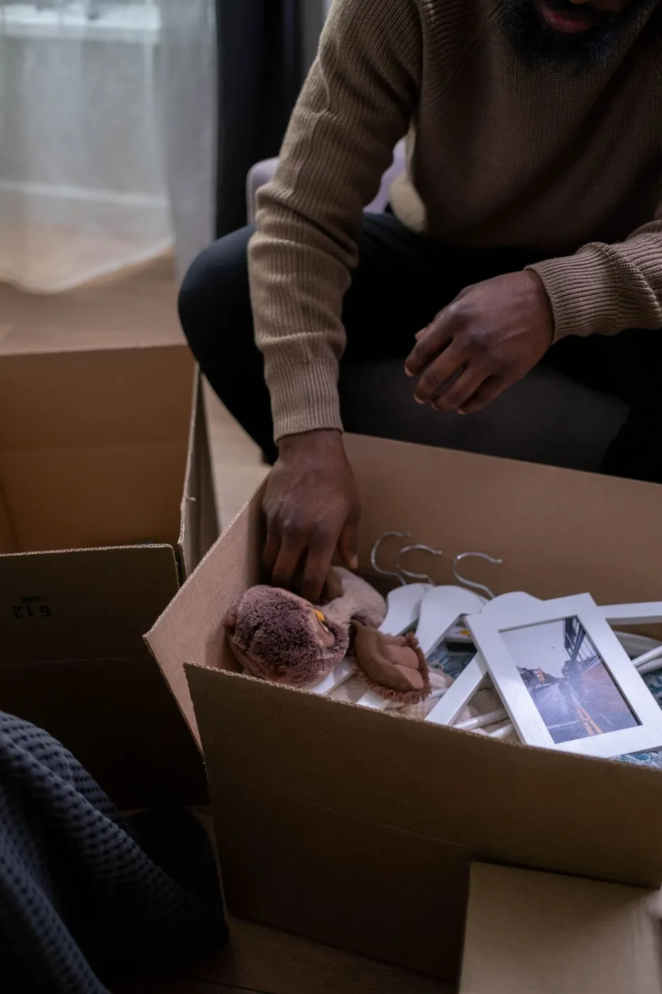 Hands sorting through an open cardboard box containing framed photographs and a pair of glasses