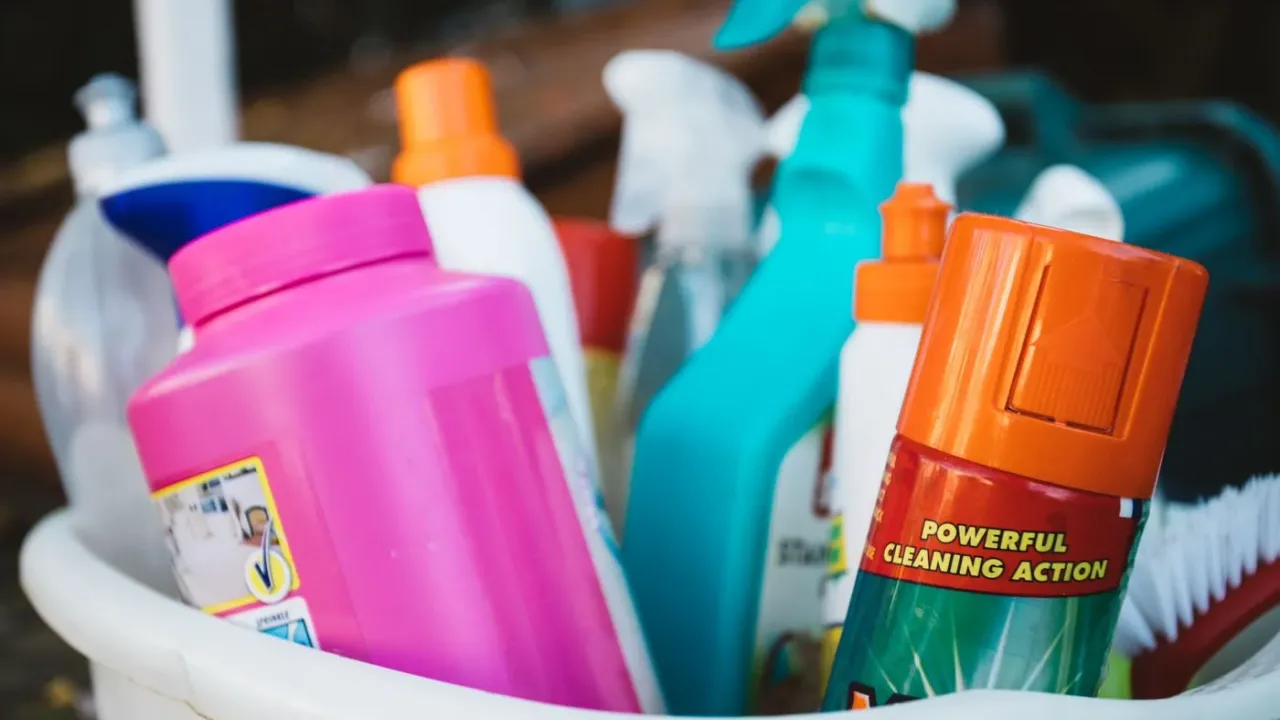 Plastic caddy packed with pink, orange, turquoise and white cleaning bottles and spray cans