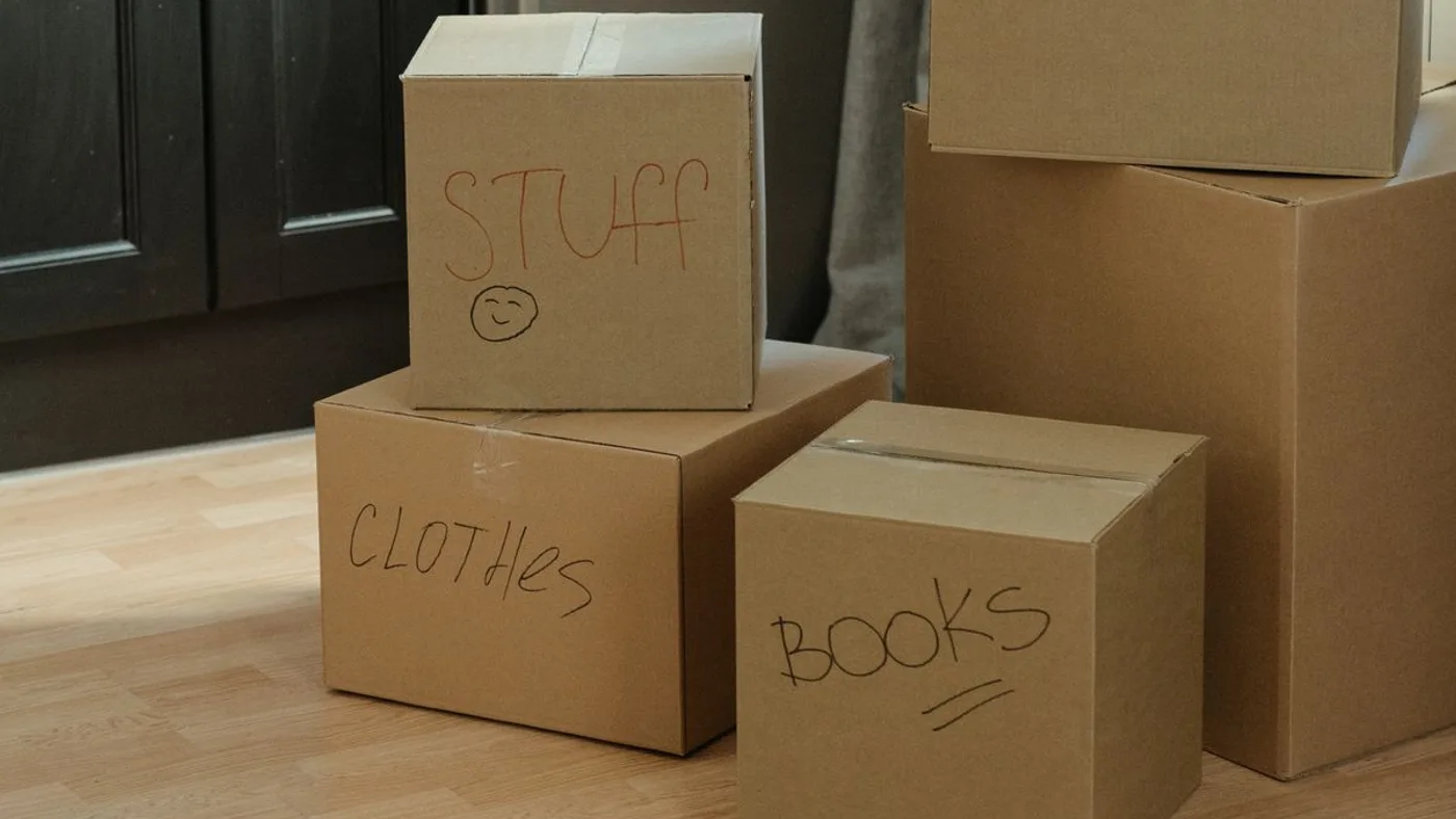 Cardboard boxes hand-labelled STUFF, CLOTHES and BOOKS in marker pen, stacked on a wooden floor
