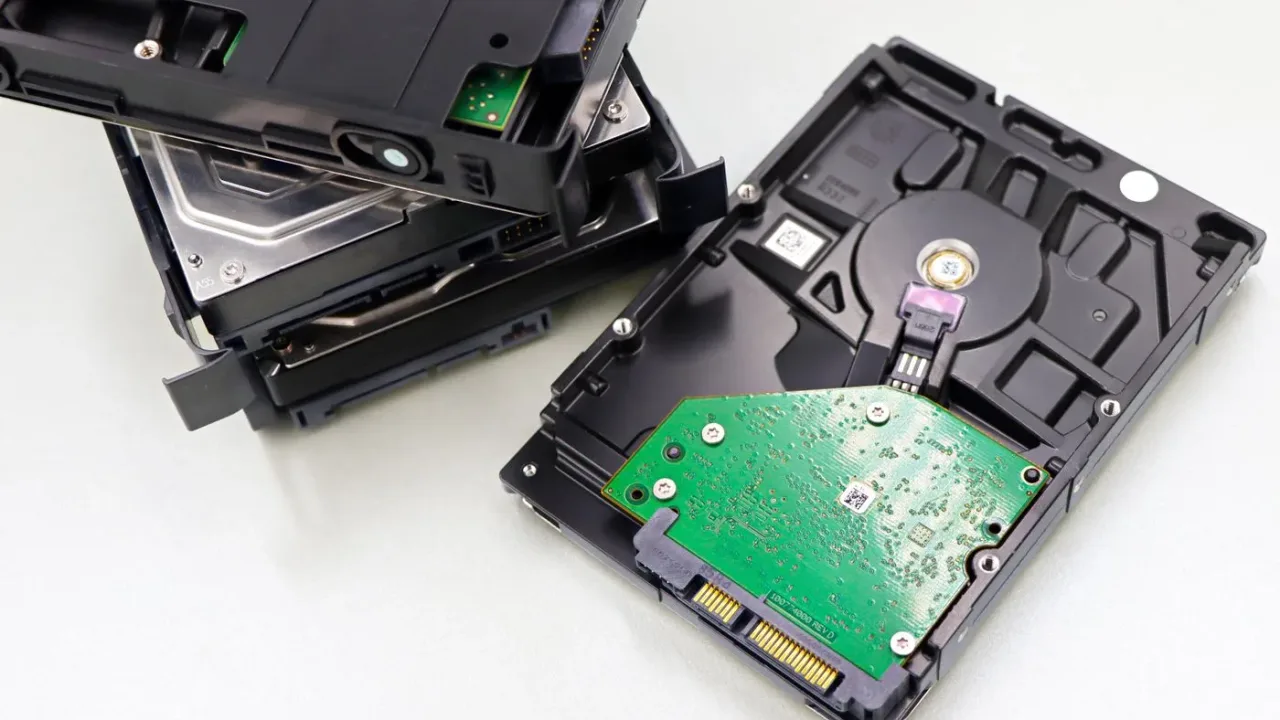 Two opened hard disk drives on a white surface, one showing its green circuit board and connector pins
