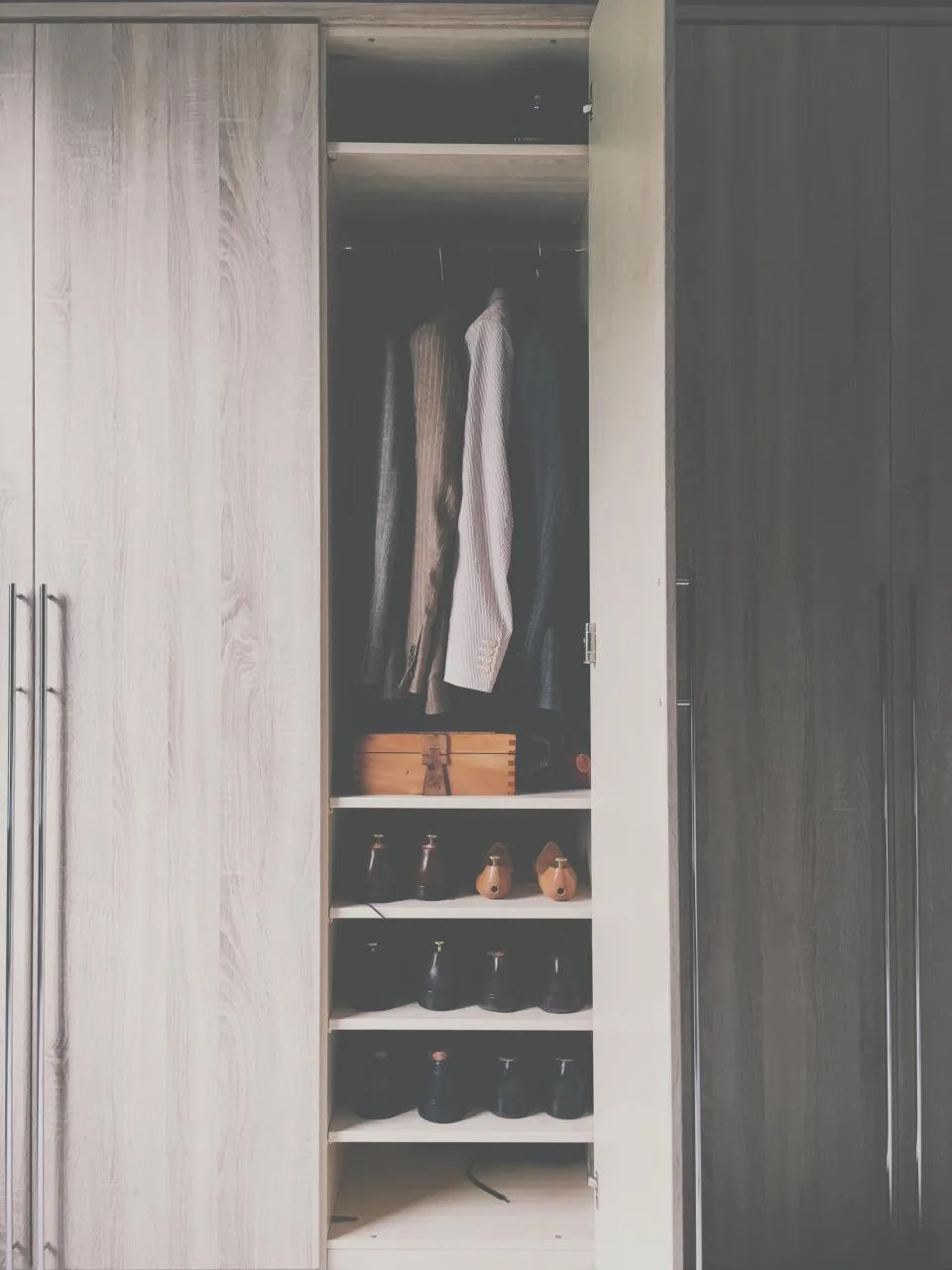 Fitted wardrobe with jackets on hangers above a small wooden keepsake box and rows of shoes
