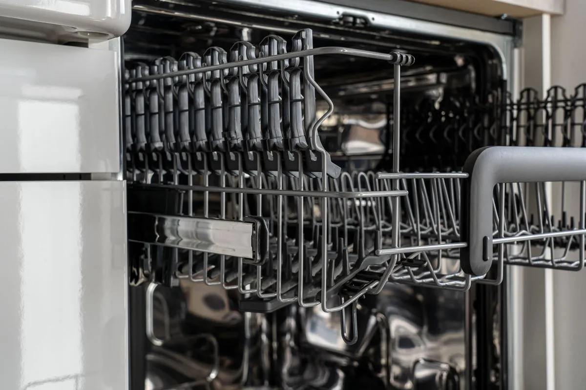 Dishwasher door fully open showing the extended upper wire rack, built into a run of white kitchen cabinetry