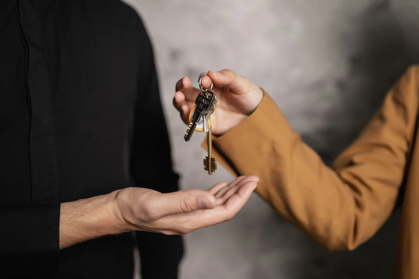 Close-up of one person dropping a set of house keys into another person's open palm against a grey wall