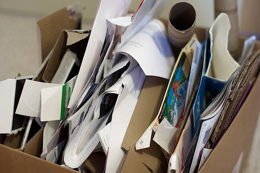 Open cardboard box filled with loose papers, printed documents, magazines and a cardboard tube ready for sorting