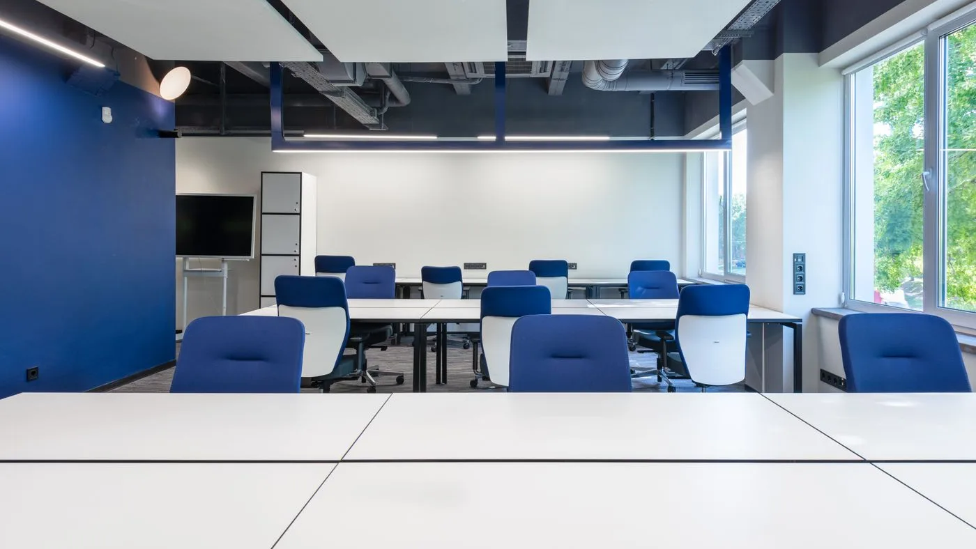 Rows of matching white office desks with blue and white task chairs in an open-plan workspace beside a large window