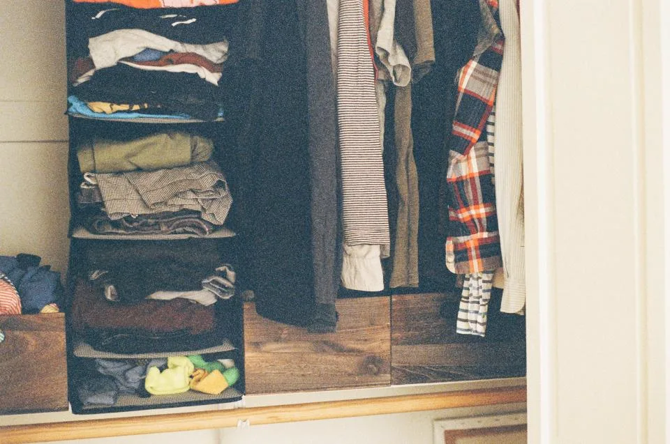 Open wardrobe shelves filled with folded clothes and garments on hangers ready for sorting