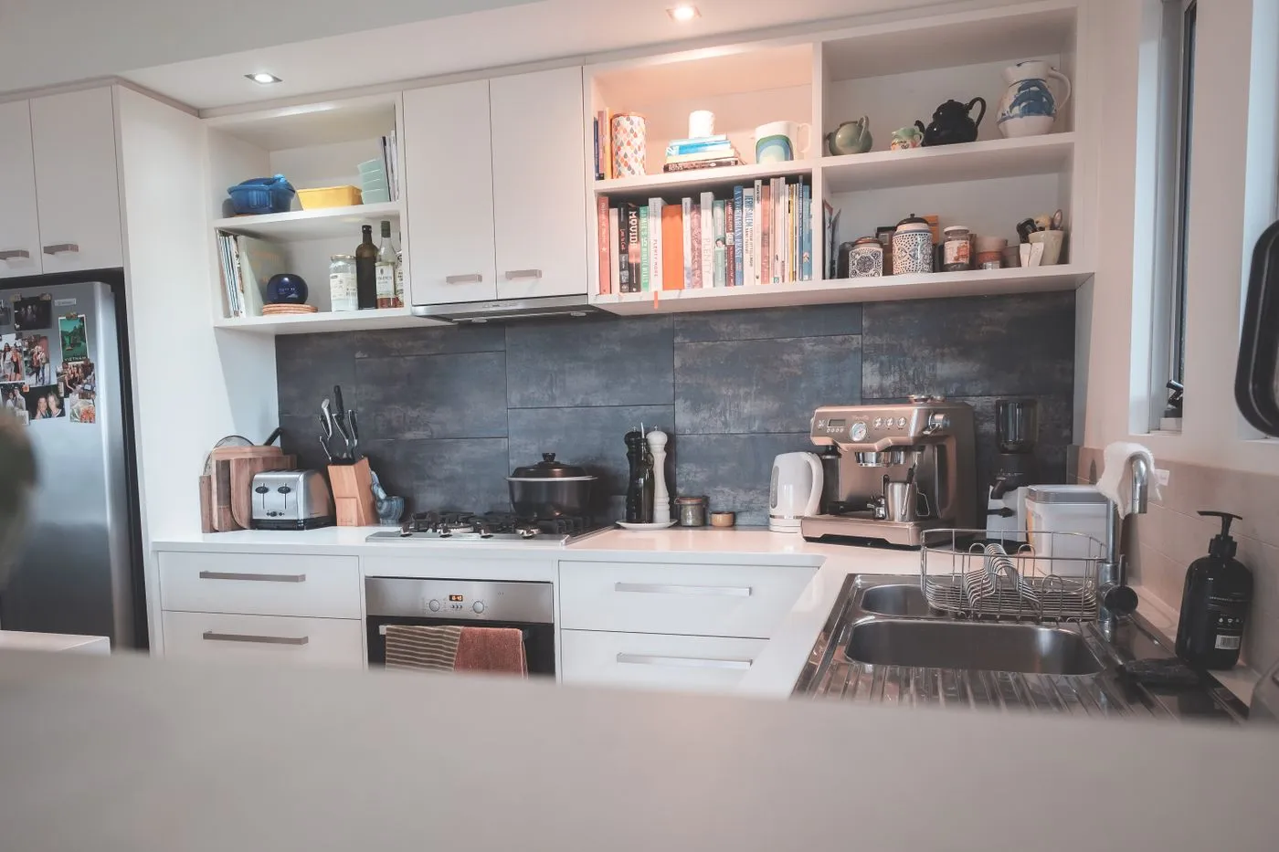 Bright modern kitchen with a stainless steel oven, gas hob, kettle, coffee machine and open shelving stacked with crockery