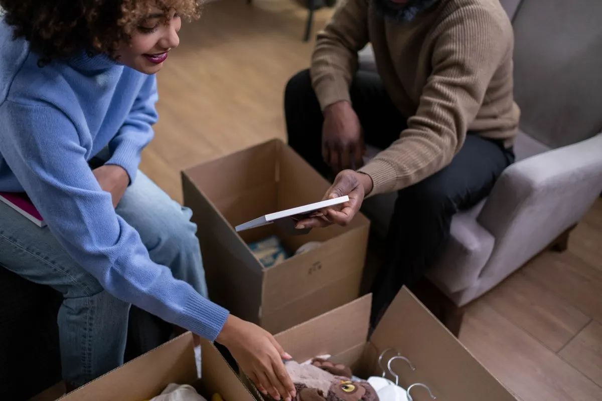Couple sitting on the floor sorting through the contents of an open cardboard box together