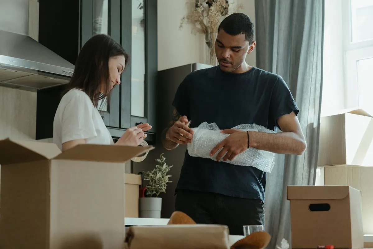 Young couple unpacking a wrapped item together in a new apartment surrounded by moving boxes