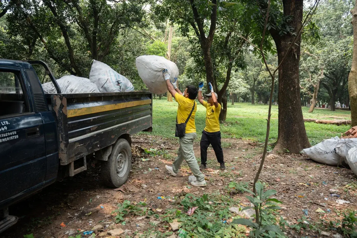 Two workers in yellow shirts lifting large waste sacks into the back of a collection truck