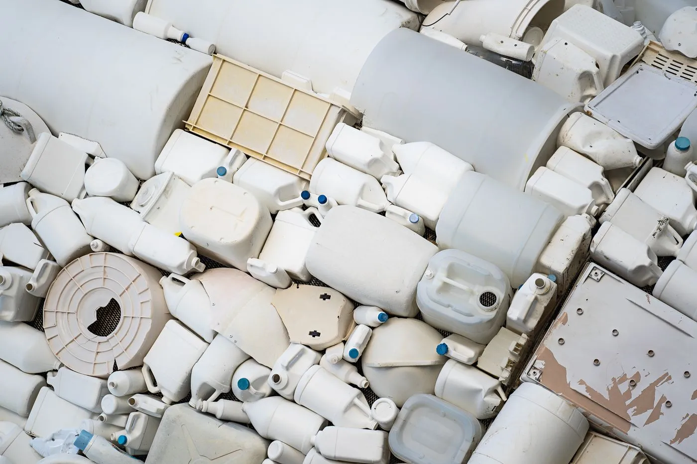 Densely stacked white plastic drums, jerrycans and containers baled together at a recycling facility