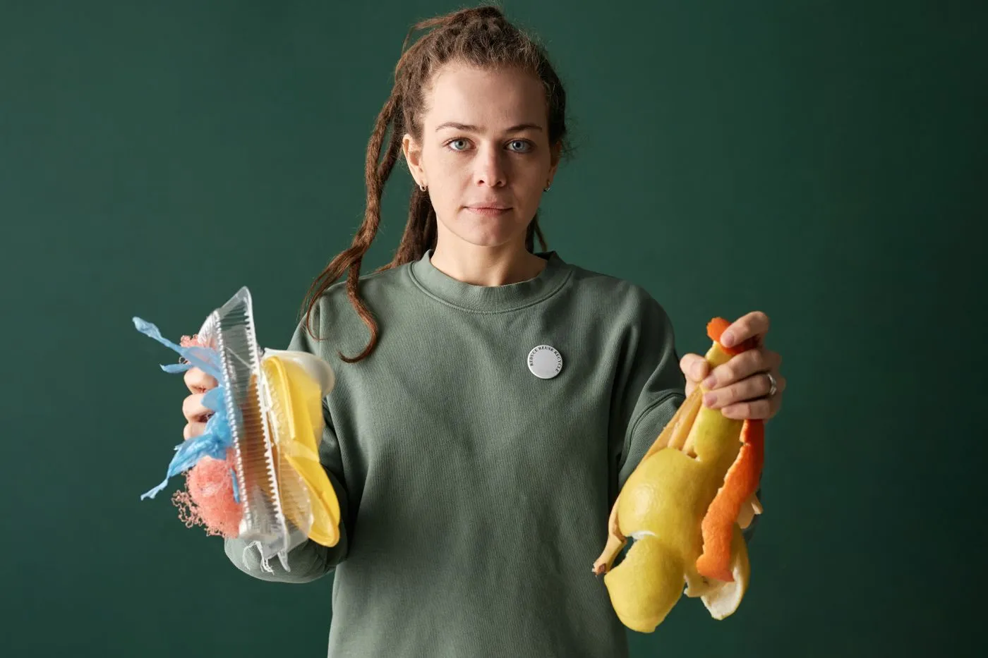 Person in a green sweatshirt holding mixed plastic packaging in one hand and lemon and orange peel in the other
