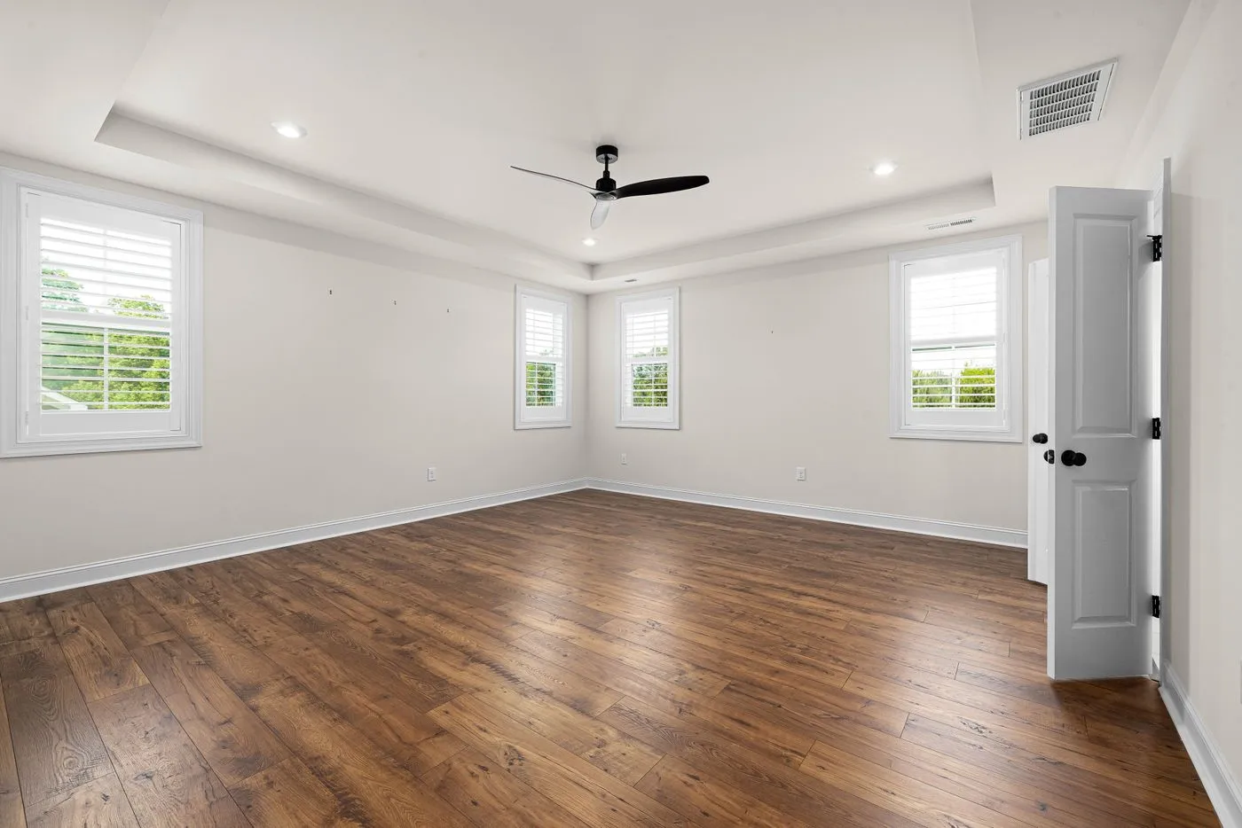 Empty room with dark wooden flooring, white walls, a ceiling fan and an open interior door