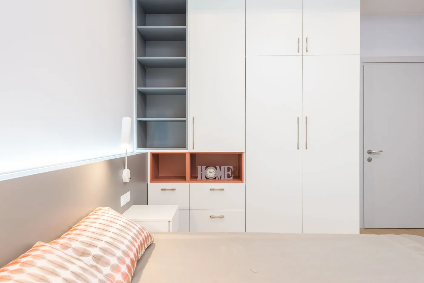 White wardrobe with shelving and drawers standing alongside a bed in a bright modern bedroom