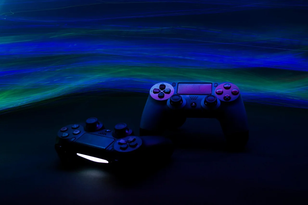 Two wireless video game controllers resting on a dark reflective desk with illuminated blue ambient lighting