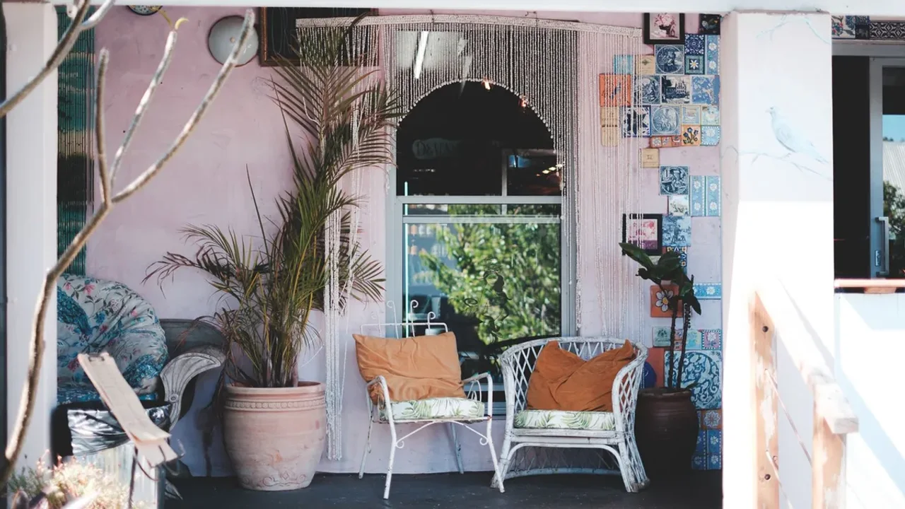 Two white outdoor chairs with orange cushions on a shaded terrace beside large plant pots