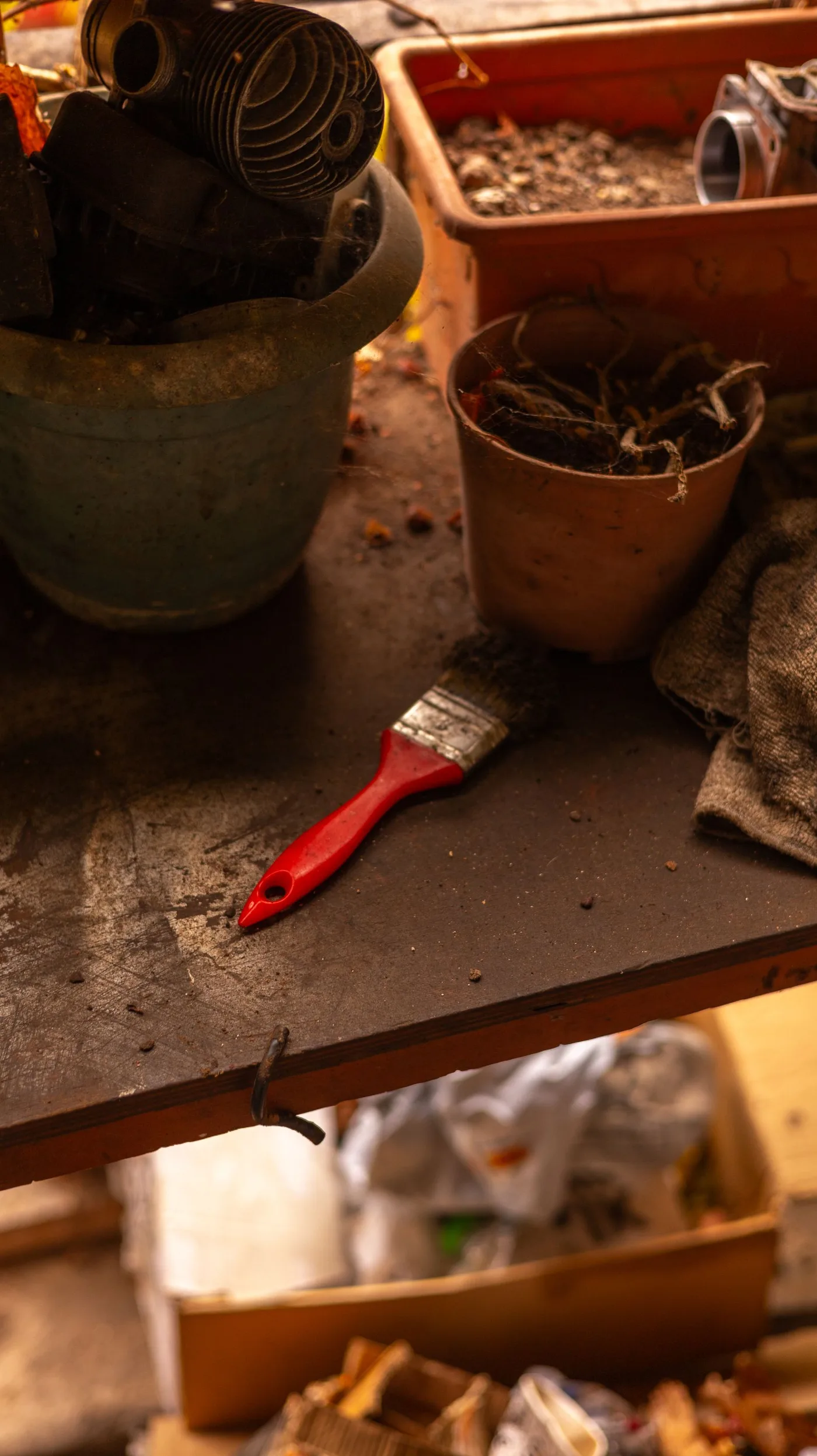 Cluttered potting bench covered with empty clay plant pots, a hand trowel and a red-handled paintbrush
