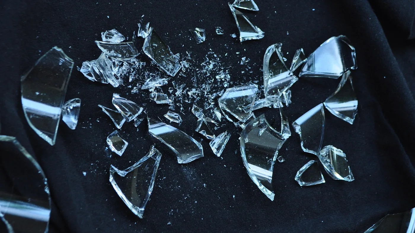 Scattered shards and splinters of clear broken glass lying across dark fabric