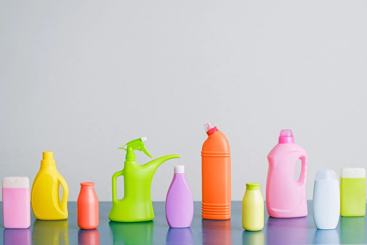 Row of brightly coloured unbranded household cleaning bottles and a spray dispenser on a reflective surface