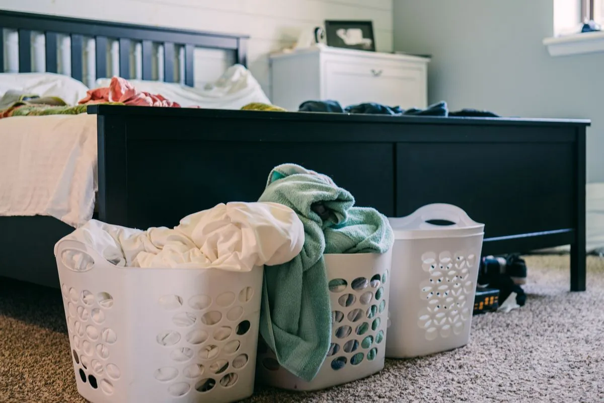 Two overflowing laundry baskets piled with folded clothing and towels at the foot of a bed