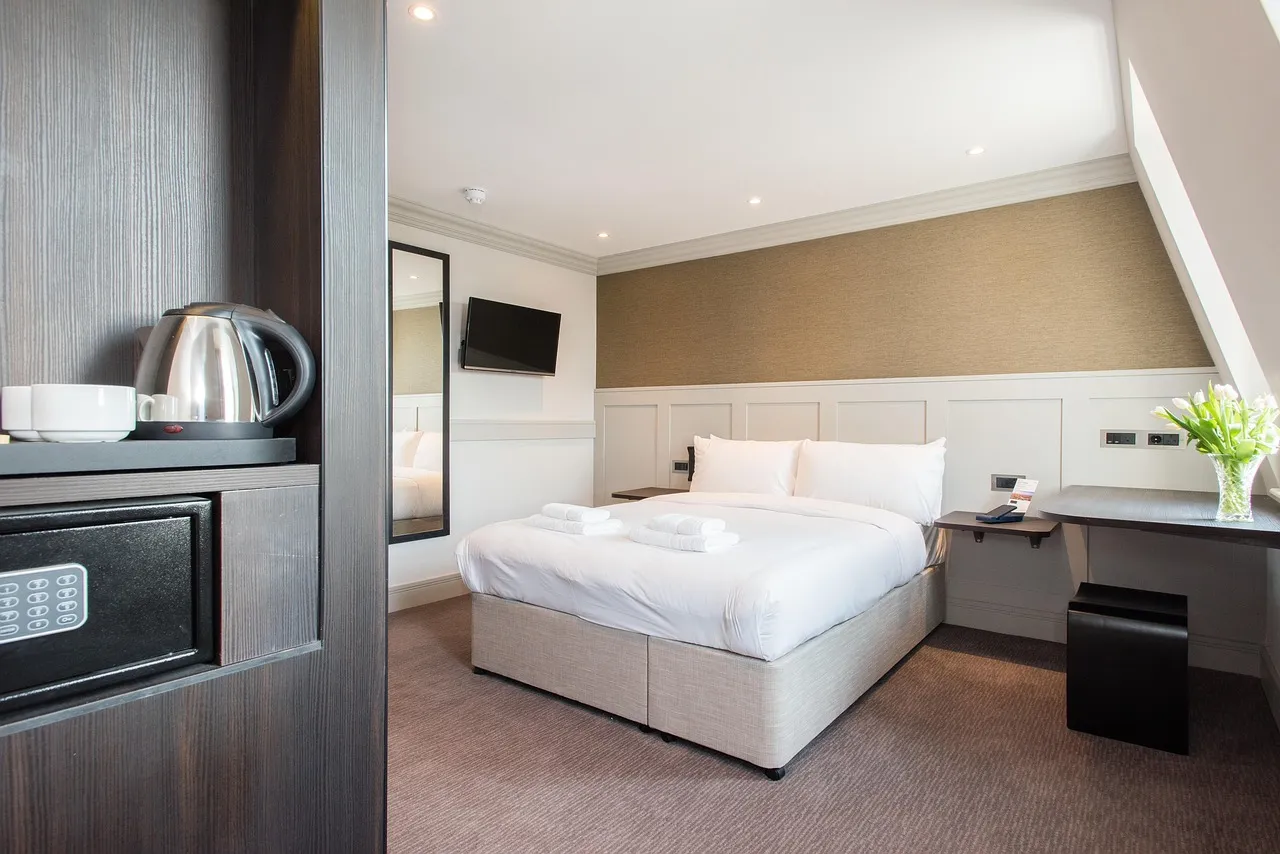 Loft-style hotel guest room with a made-up bed, wall-mounted television, work desk and in-room safe
