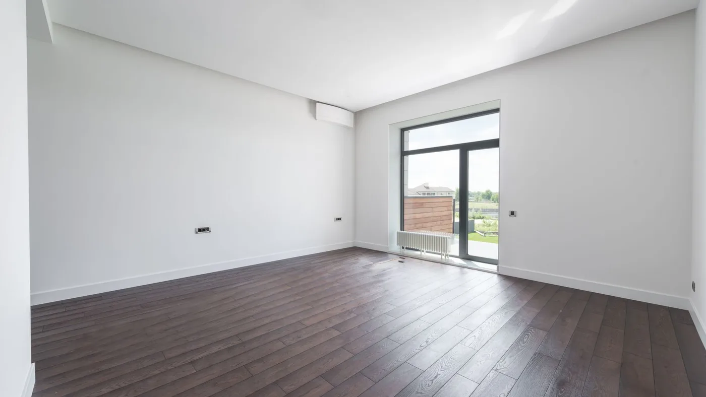 Empty room with white walls, dark wood flooring, a wall-mounted split air conditioning unit and a glazed balcony door