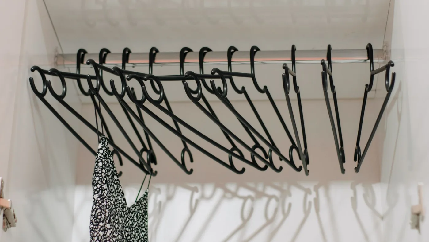 Row of black wire coat hangers on a wardrobe rail with a single patterned dress left hanging in an otherwise emptied wardrobe