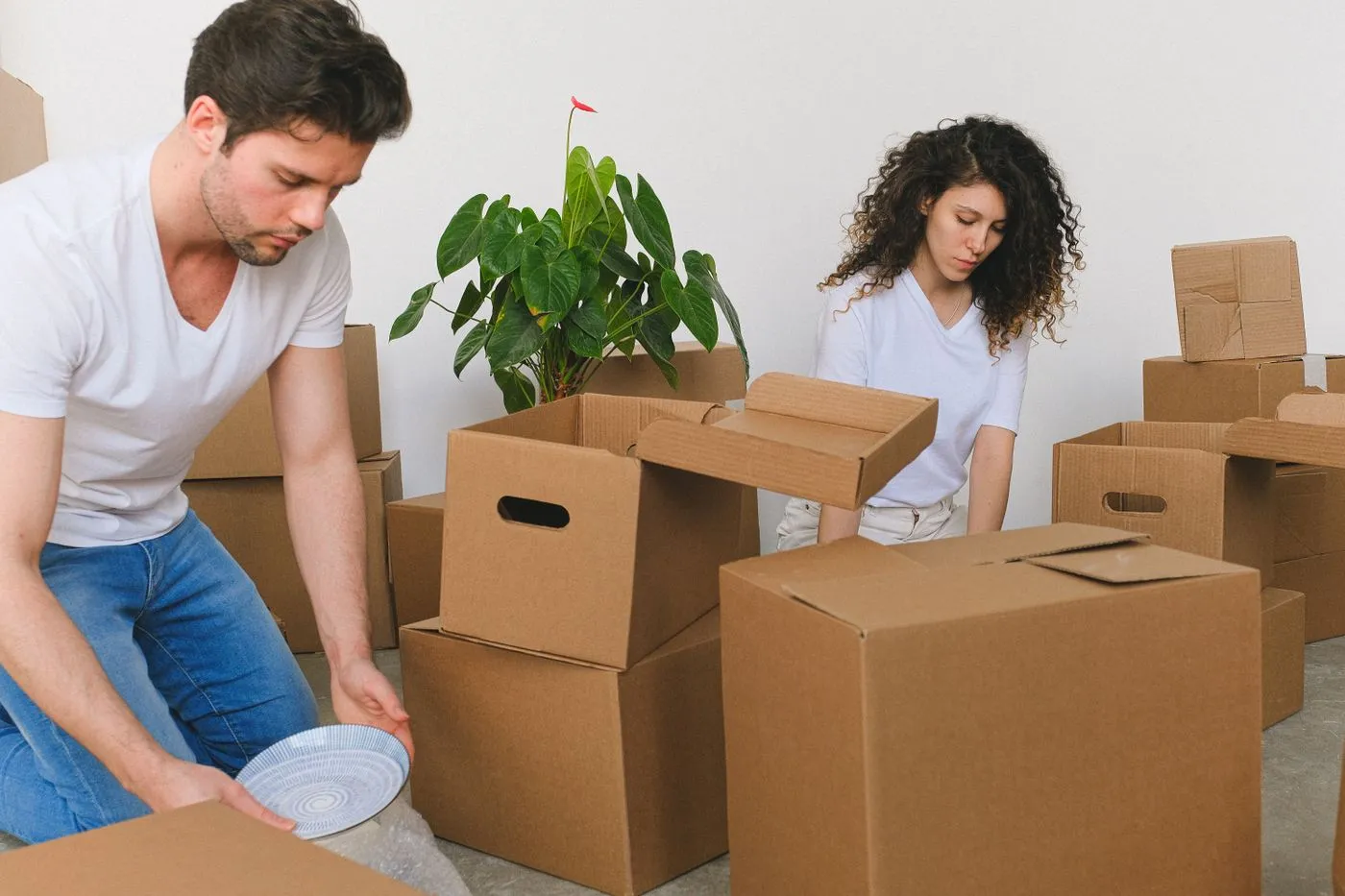 Couple kneeling among cardboard moving boxes wrapping plates in a nearly empty living room