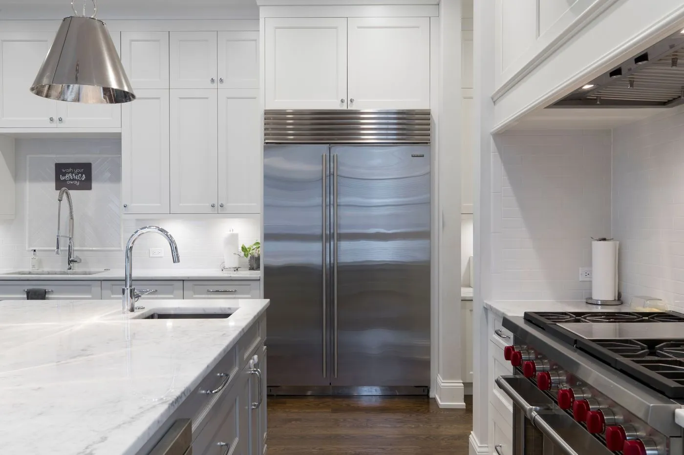 Large stainless steel side-by-side refrigerator built into a white fitted kitchen with marble worktops