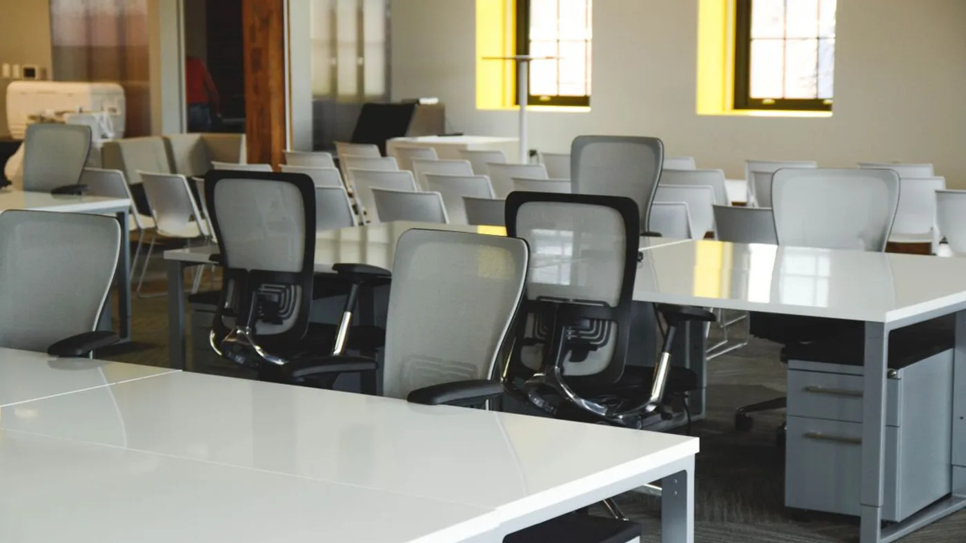 Rows of white bench desks with grey mesh task chairs, stacking chairs and mobile pedestal units in an open-plan office
