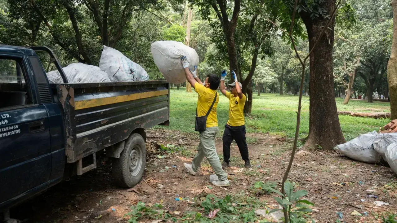 Waste management collection crew in high-visibility uniforms loading waste sacks into the back of a collection truck